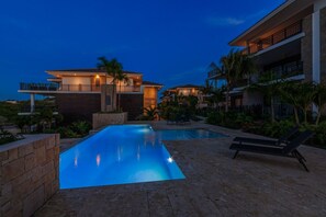 A modern resort with a swimming pool, lounge chairs, and a well-maintained garden.