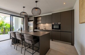 Una cocina moderna con una isla central, taburetes de bar, iluminación colgante y vistas al exterior.