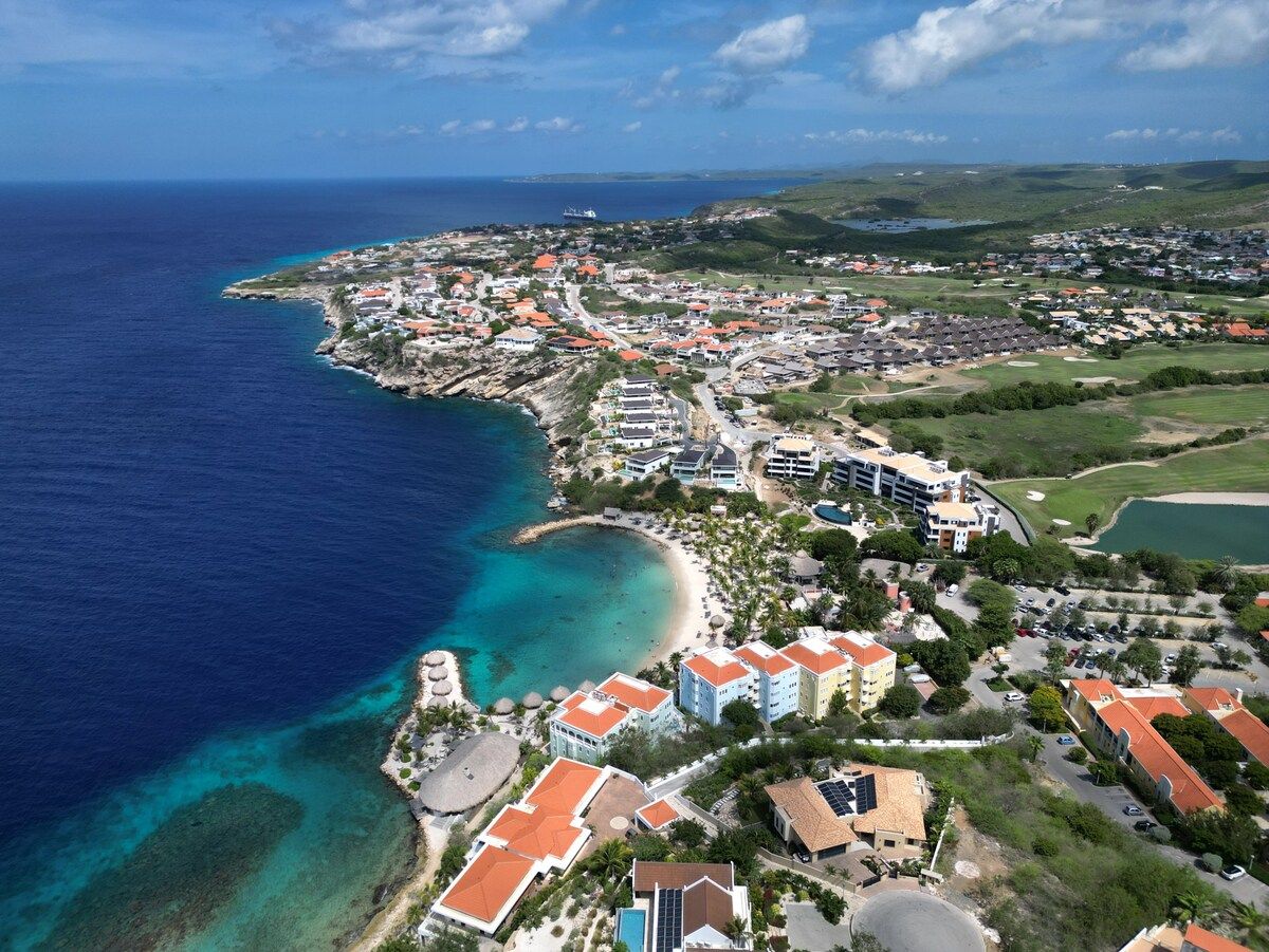 Vista aérea de uma cidade costeira com praia, edifícios e um campo de golfe.