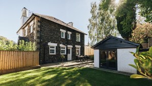 A two-story stone house with a small attached shed, a well-maintained lawn, and a patio area with outdoor furniture.