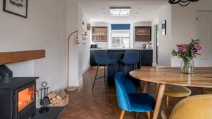 A cozy living room with a fireplace, a dining area with blue chairs, and a kitchen with wooden cabinets and a blue countertop.