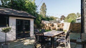 A patio with a wooden table and chairs, a potted plant, and a small shed.
