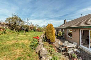 Ett hus med en trädgård som har en mur av sten, en uteplats med ett bord och stolar samt utsikt över det omgivande landskapet.