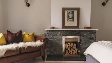 A cozy living room with a stone fireplace, a framed picture above it, and a brown leather sofa with colorful cushions.
