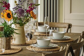 Enjoy a warm and inviting dining experience with a beautifully set table featuring a vase with fresh flowers, woven placemats, and fine glassware.