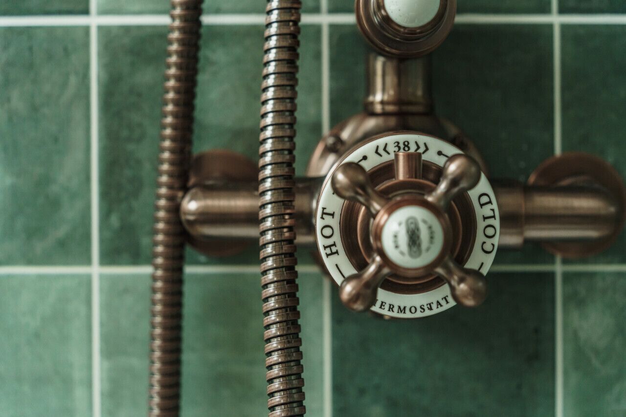 A bathroom with a green tiled wall and a brass faucet with a temperature control dial.