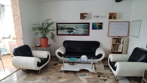 Een woonkamer met een zwart-wit bank, twee fauteuils, een salontafel, een potplant, een schilderij en een whiteboard.