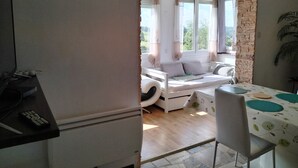 Een kamer met een bed, een tafel met een bloemenkleed, een stoel en een raam met gordijnen.