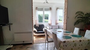 Een eethoek met een tafel voor vier personen, een zwarte lederen stoel en uitzicht op een tuin door grote ramen.