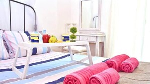 Ein ordentlich bezogenes Bett mit rosa Handtüchern, einer gestreiften Bettdecke und einem kleinen Tisch mit Früchten und einer Tasse.