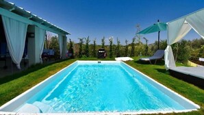 Ein rechteckiger Swimmingpool mit glasklarer, blauer Wasserfläche, umgeben von einer gepflegten Rasenfläche und weißen Gartenmöbeln.