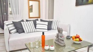 Ein modernes Wohnzimmer mit einem weißen Sofa, gestreiften Kissen, einem Glastisch mit Dekoration und einer Obstschale.