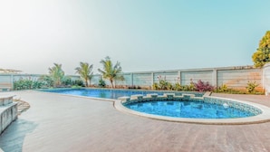 A swimming pool with a tiled edge, surrounded by a paved deck and palm trees.