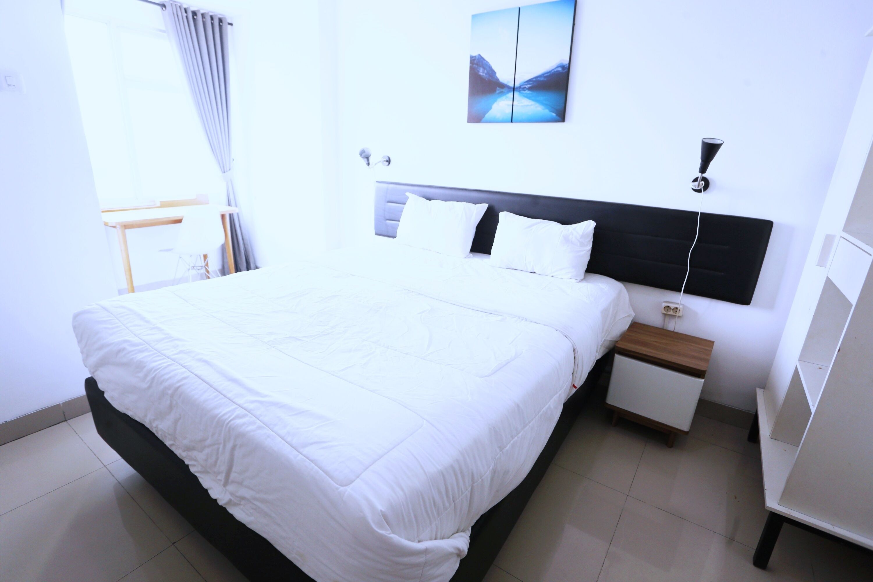 A neatly made bed in a hotel room with a modern headboard, a bedside table, and a wall-mounted lamp.