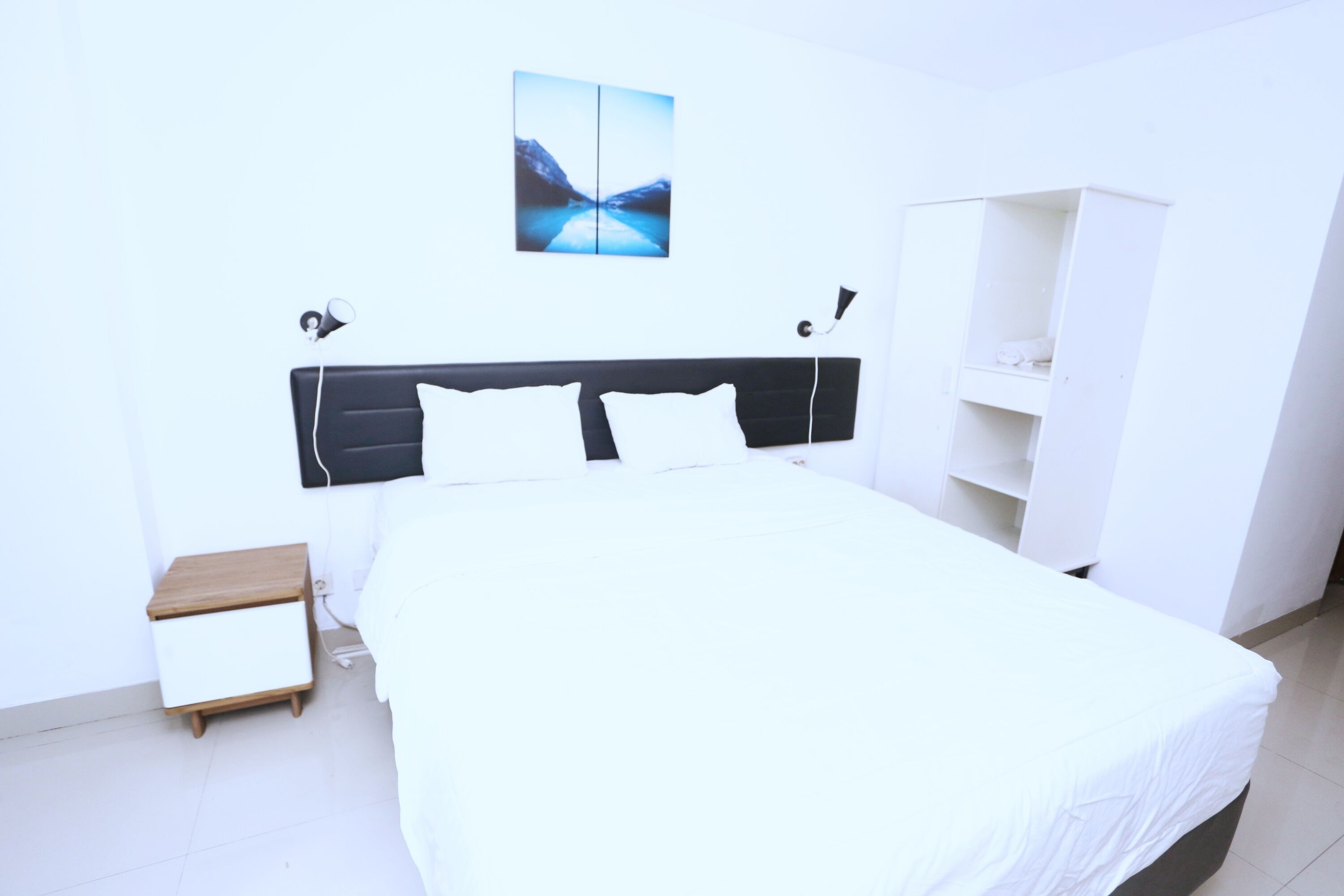 A modern bedroom with a large bed, a bedside table, a wardrobe, and a wall-mounted artwork.