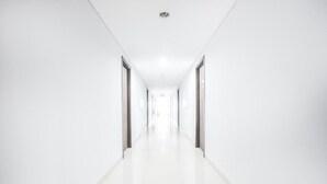 A long, narrow hallway with white walls and a shiny floor, leading to a bright exit.