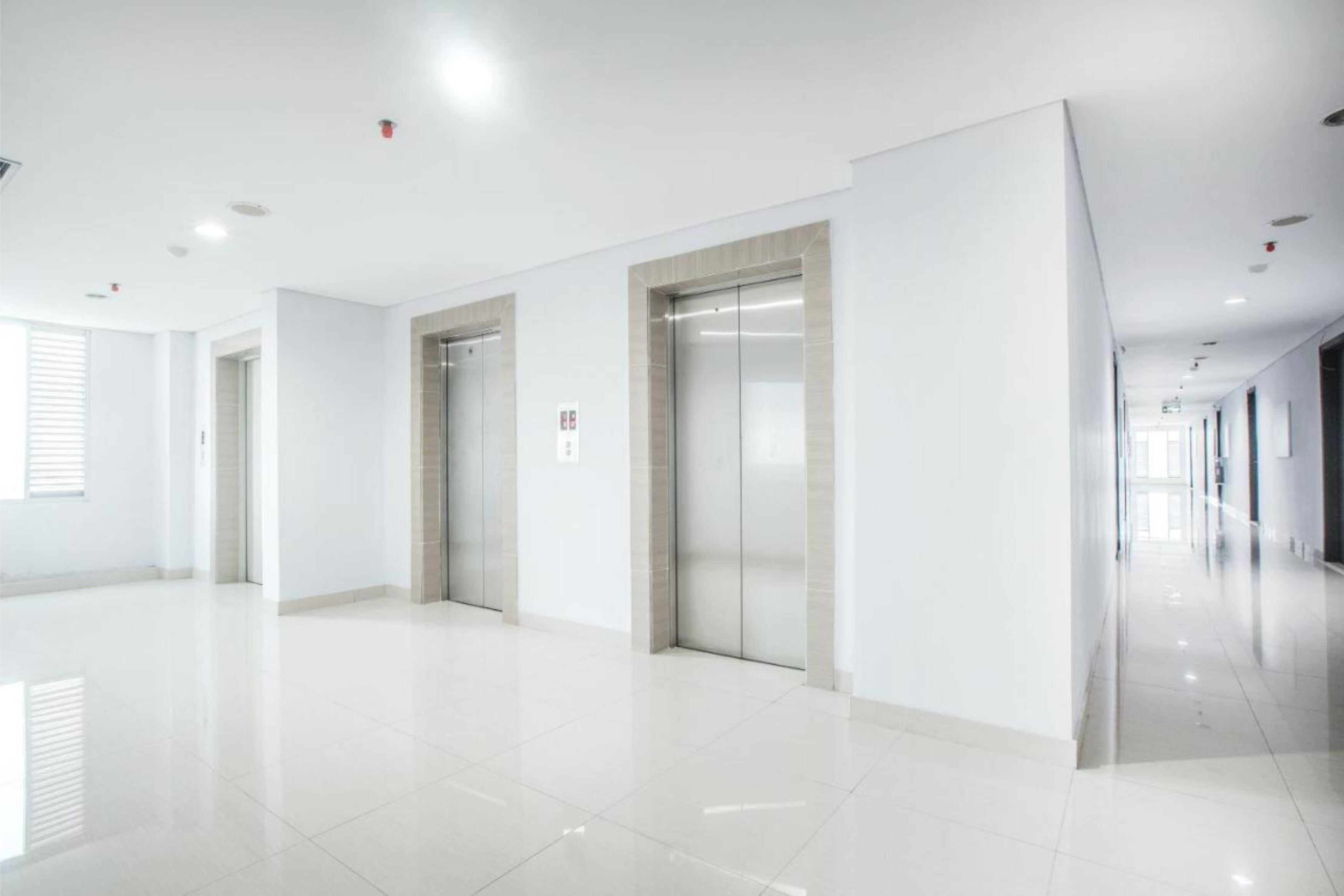 A spacious, modern hallway with two elevators and a clean, reflective floor.