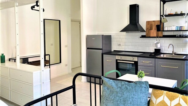 A modern kitchen with white cabinets, a black refrigerator, and a black stove. There is a dining area with a table and chairs. - Contemporary studio- Ornato 13 (Milan)
