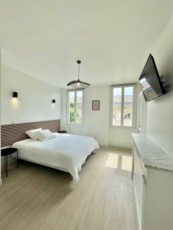 Relax in a spacious bedroom with a large bed, flat-screen TV, and natural light pouring in through two windows.