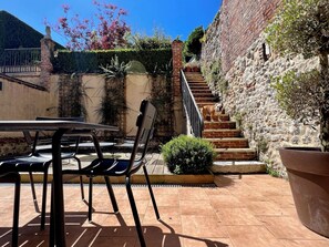 En terrasse med et bord, stole, en trappe og en stenvæg.