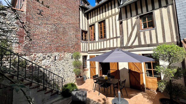 A courtyard with a stone staircase, a wooden table with chairs, and a potted plant. - La Terrasse du 10 Honfleur (Honfleur)