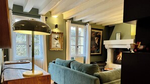 A cozy living room with a green sofa, a wooden side table with a lamp, a fireplace, and framed artwork on the walls. - La Terrasse du 10 Honfleur (Honfleur)