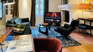A living room with a sofa, armchair, coffee table, and a flat-screen TV displaying a movie. - La Terrasse du 10 Honfleur (Honfleur)