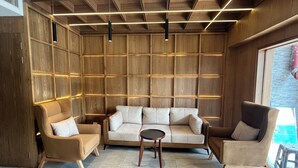 Un salon moderne avec un canapé d’angle, deux fauteuils et une petite table ronde. La pièce est dotée de lambris en bois sur les murs et d’un plafond en pente avec un éclairage intégré.