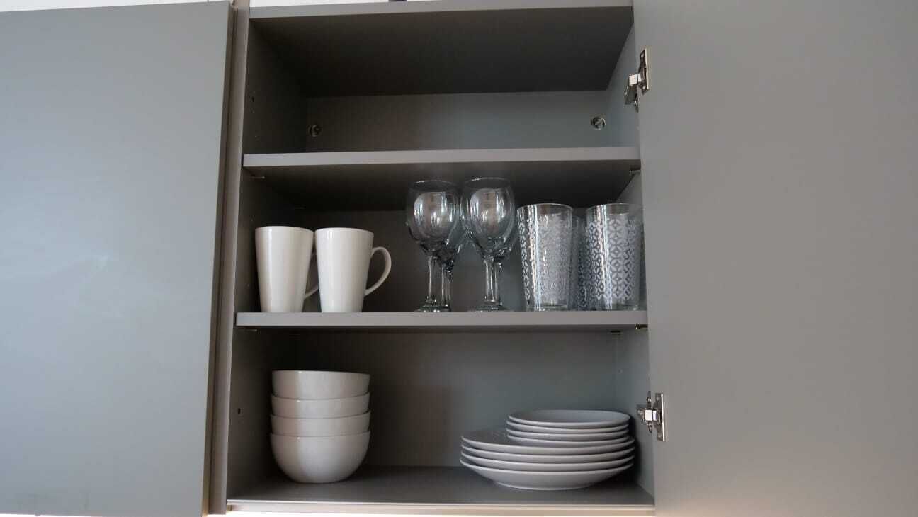 Un mueble con estantes que contiene tazas blancas, copas de vino y cristalería decorada.