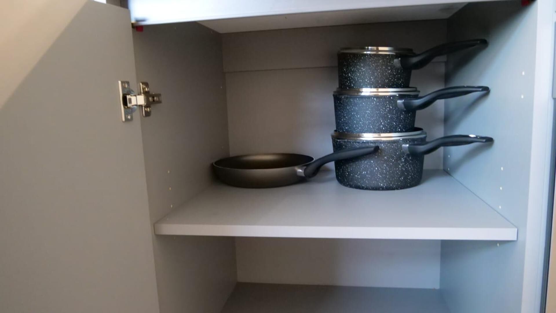 Uma cozinha com uma prateleira branca que acomoda uma frigideira e três panelas empilhadas.