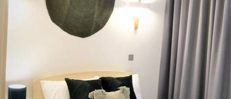 A hotel room with a bed, a round wall decoration, a nightstand with a lamp, and a window with curtains.