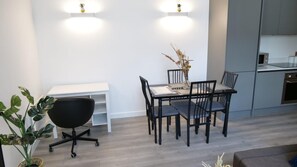 Een moderne eetruimte met een witte tafel, zwarte stoelen en een vaas met gedroogde planten.