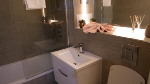 Een moderne badkamer met een douchecabine van glas, een witte wastafel met één kraan en een toilet.