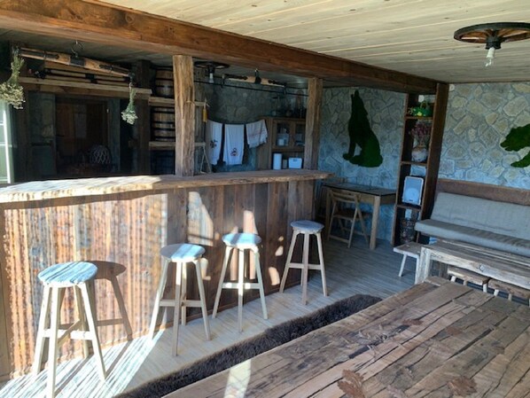 Un coin bar au style rustique, avec des tabourets en bois, un mur en pierre orné d’une fresque représentant un loup et un banc.