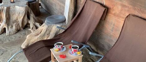 A wooden cabin with two reclining chairs, a small table with cups and a lemon, and a window.