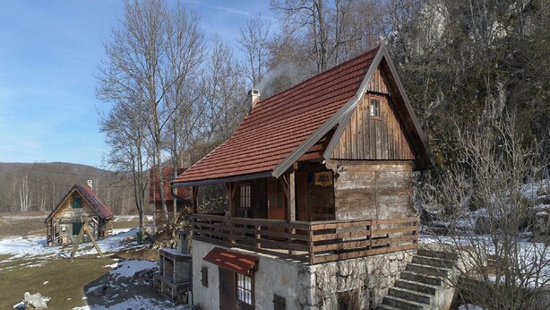 A rustic wooden cabin with a red roof, a wooden porch, and a stone staircase leading to the entrance. - Holiday Home Jela (Gospic)