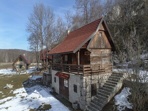 A rustic wooden cabin with a red roof, a wooden porch, and a stone staircase leading to the entrance. - Holiday Home Jela (Gospic)