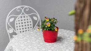 Une table recouverte d’une nappe en dentelle blanche, un pot rouge contenant des fleurs et une chaise en métal blanc dotée d’un dossier décoratif.