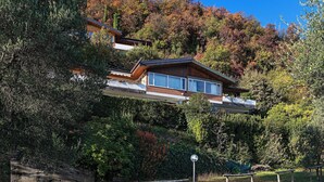 A modern house with a sloped roof, large windows, and a view of a forested hillside. - Residence San Giorgio by Wonderful Italy (Toscolano Maderno)