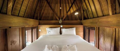 A wooden cabin room with a large bed, wooden walls, and a sloped ceiling.