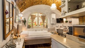 A bedroom with a large bed, a window with stained glass, a wooden ceiling, and a kitchen area with a stove and cabinets. - C'era una volta in centro by Wonderful Italy (Desenzano del Garda)