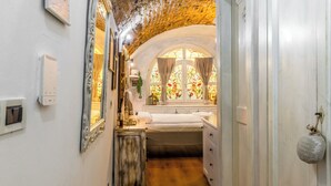 A narrow hallway with a wooden floor leading to a room with a bed, a window with stained glass, and a door with a round object hanging on it. - C'era una volta in centro by Wonderful Italy (Desenzano del Garda)
