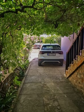 A white car parked in a narrow driveway with a stone wall on one side and a staircase on the other.
