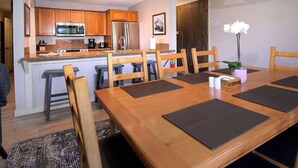 A modern kitchen with wooden cabinets, a stainless steel refrigerator, and a dining area with a wooden table and chairs. - Ponderosa Place, Walk to slopes, Hot tub! (Mt. Crested Butte)
