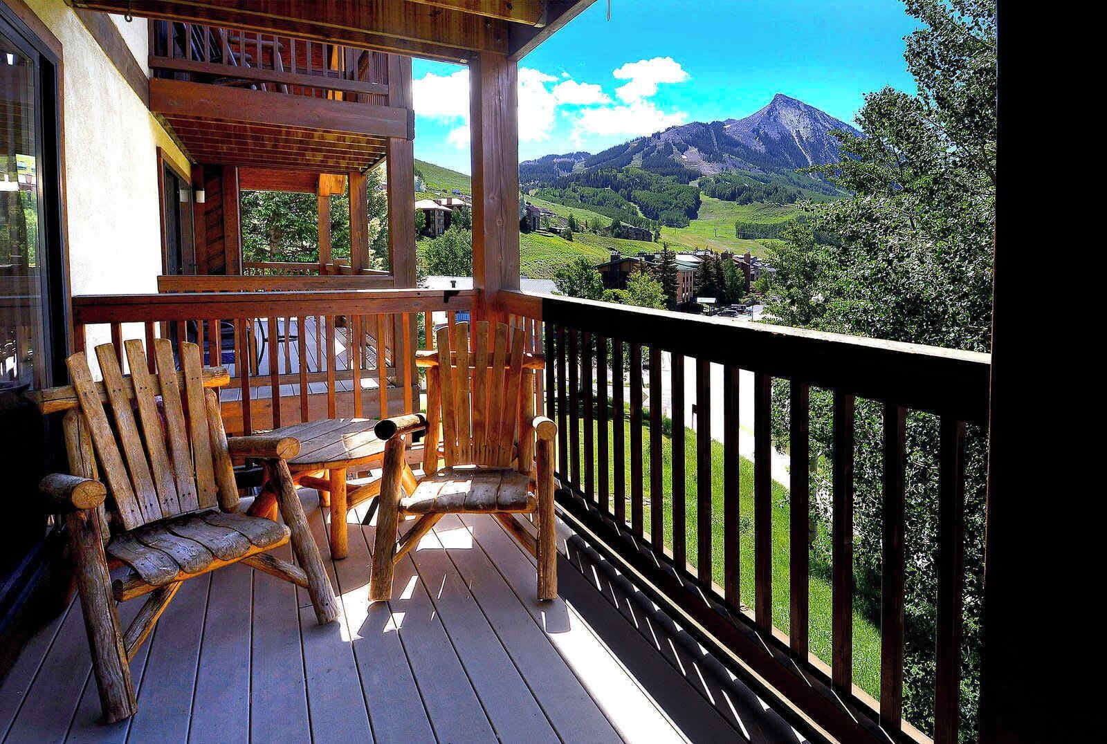 Une terrasse en bois avec une table et des chaises, une balustrade et un paysage montagneux en arrière-plan.