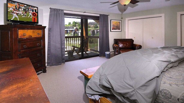 A bedroom with a bed, a dresser, a chair, a television, and a balcony with a view of the outside. - Ponderosa Place, Walk to slopes, Hot tub! (Mt. Crested Butte)