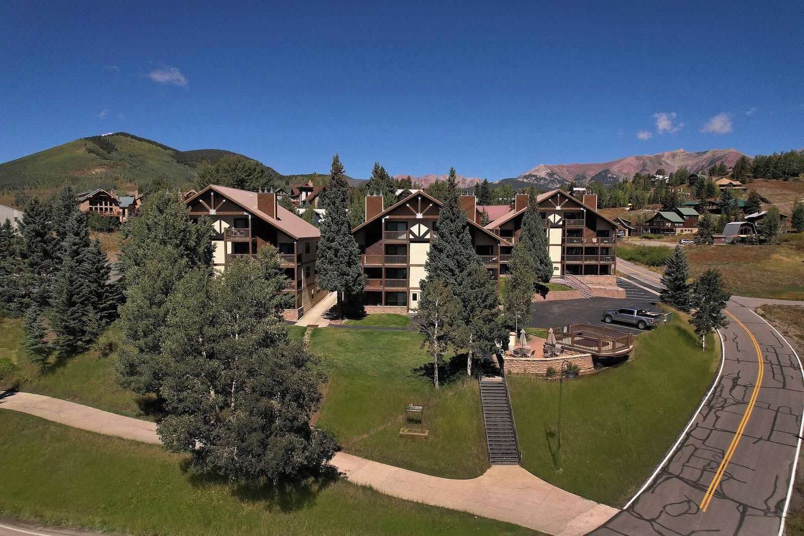 A multi-story lodge with a central courtyard, surrounded by trees and a mountain backdrop.