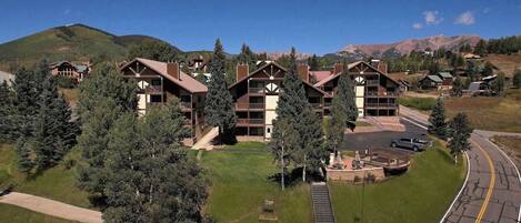 A multi-story lodge with a central courtyard, surrounded by trees and a mountain backdrop.