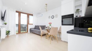A modern kitchen with white cabinets, a dining area with a table and chairs, and a gray sofa.