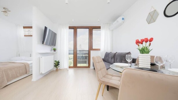 A modern apartment with a dining area, a sofa, a TV, and a balcony with a view.